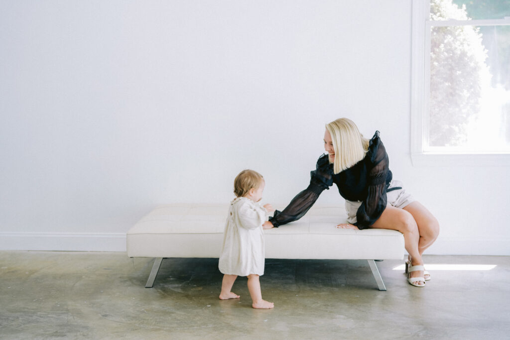 Image of a luxury wedding photographer sitting on a white sofa with her young daughter walking towards her