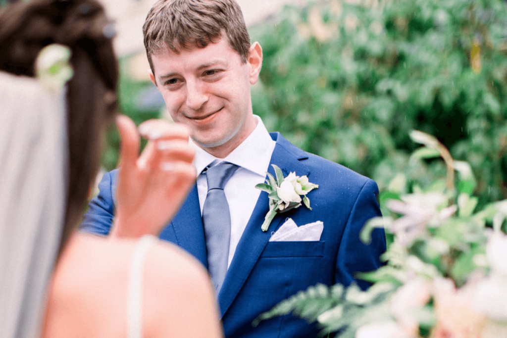 Image of a groom wearing a blue suit looking lovingly at his wife. This is showing an example of an energetic image from a wedding photographer shot list
